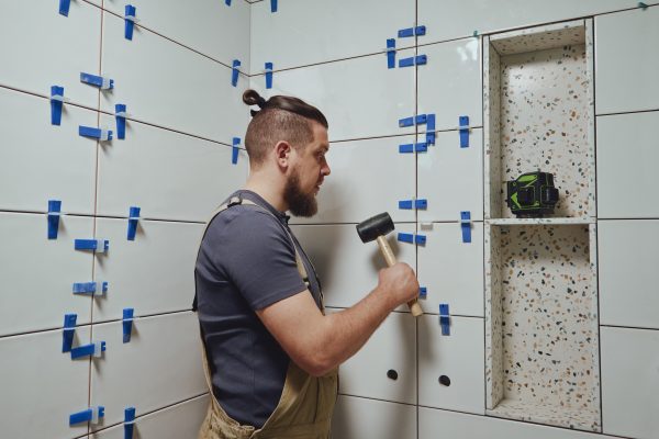 Tiler knocks the wedges of the ceramic tile leveling system off the wall in the bathroom.
